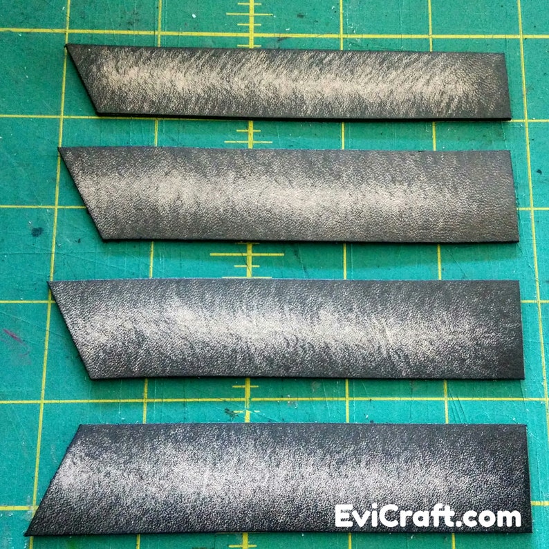 May include: Four rectangular, dark gray leather strips with angled ends. Each strip has a textured, distressed appearance with lighter gray highlights. The strips are arranged parallel against a green grid background.