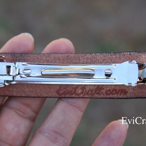 May include: A brown leather barrette with a silver metal clasp. The barrette has a rectangular shape and is designed for securing hair. The text "EviCraft.com" is visible on the bottom right.