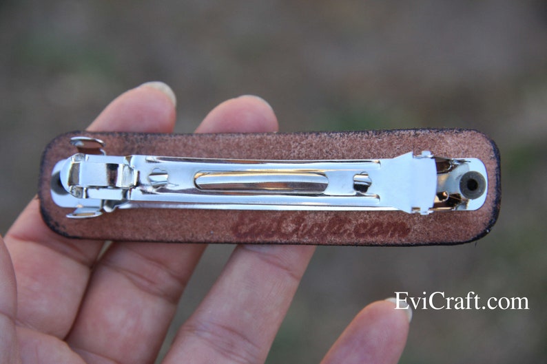May include: A brown leather barrette with a silver metal clasp. The barrette has a rectangular shape and is designed for securing hair. The text "EviCraft.com" is visible on the bottom right.