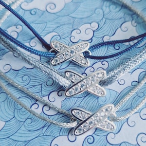 Peut inclure: Trois bracelets argentés avec des cordons bleus et gris. Chaque bracelet est orné d'un charme argenté en forme d'avion avec des cristaux transparents.