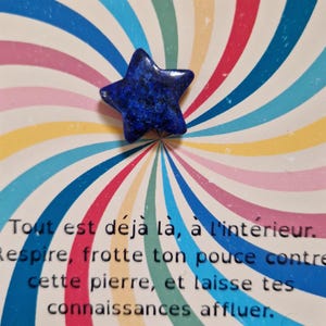 Op de afbeelding: Een donkerblauwe, stervormige edelsteen ligt op een kaart met een kleurrijk spiraalontwerp. De kaart heeft Franse tekst. De edelsteen is diepblauw met een getextureerd oppervlak. Het thema is spiritueel of metafysisch.