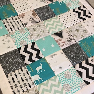 May include: A patchwork quilt with a variety of patterns in shades of gray, white, and teal. The quilt features a variety of designs, including stars, arrows, deer, and geometric patterns.