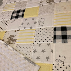 May include: A yellow and grey patchwork baby quilt featuring a Winnie the Pooh character design. The quilt is made from various fabrics with different patterns, including stars, polka dots, stripes and plaid.