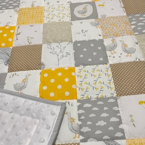 May include: A patchwork baby quilt with a white background and yellow, brown, and grey squares. The quilt features a repeating pattern of geese and floral designs. The quilt is made of soft, comfortable fabric and is perfect for cuddling.