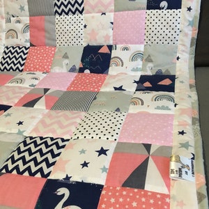 May include: A patchwork baby quilt with a variety of patterns, including stars, rainbows, swans, and mountains. The quilt is made in shades of pink, blue, white, and gray.