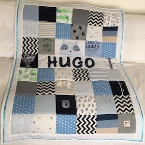 Könnte beinhalten: Eine blaue und weiße Patchwork-Babydecke mit einem niedlichen Panda-Applikationen und dem Namen "HUGO", der in Schwarz gestickt ist. Die Decke besteht aus verschiedenen Stoffen, darunter Denim, Flanell und Baumwolle.