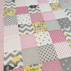 Könnte beinhalten: Eine rosafarbene und graue Patchwork-Babydecke mit verschiedenen Mustern, darunter Punkte, Herzen und Elefanten.