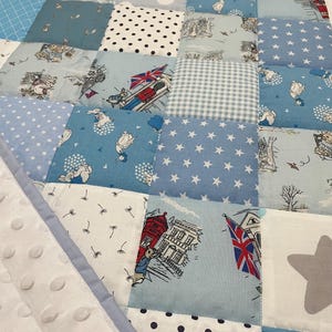 Könnte beinhalten: Eine blaue und weiße Patchwork-Babydecke mit verschiedenen Mustern, darunter Sterne, Punkte und ein Peter Rabbit-Design.