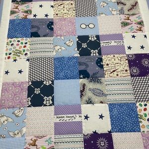 May include: A patchwork quilt with a Harry Potter theme. The quilt is made of various fabrics with different patterns, including stars, owls, glasses, and the Hogwarts crest. The quilt is also decorated with the text "Mischief Managed" and "Expecto Patronum".