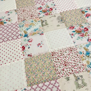 May include: A patchwork quilt with a variety of floral and geometric patterns in pink, white, and green. The quilt is made of squares of different fabrics sewn together.