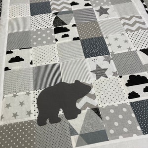May include: A black and white patchwork baby playmat with a bear silhouette in the center. The playmat features various patterns including stars, clouds, polka dots, stripes, and zigzags.