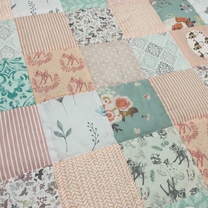 Può includere: Una trapunta patchwork con una varietà di motivi in ​​tinte di rosa, verde e bianco. La trapunta presenta una stampa di cervo, una stampa floreale e motivi geometrici.