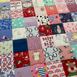 May include: A patchwork quilt composed of various fabric squares, featuring diverse patterns and colors. Some squares display text like "Lucia," "Daddy is the Best," and "Lucia's First Eurovision." The quilt includes images of penguins, owls, rainbows, and other playful designs.