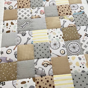 Könnte beinhalten: Eine Patchwork-Decke mit verschiedenen Mustern und Farben, darunter Braun, Grau, Weiß und Gelb. Die Decke zeigt ein Auto-, Fahrrad- und Schraubenschlüssel-Design.