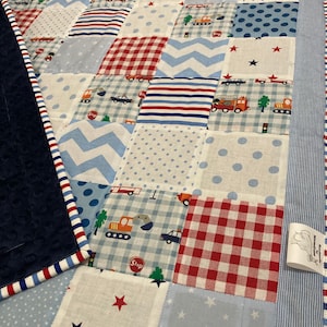 May include: A patchwork quilt with a blue and white color scheme. The quilt is made up of various squares with different patterns, including stars, stripes, polka dots, and checkered patterns. The quilt is bordered with a blue and white striped fabric.