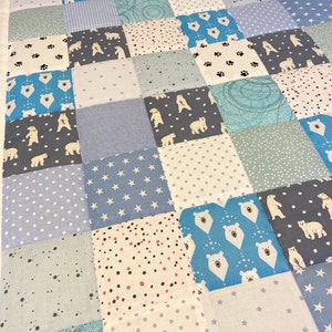 Könnte beinhalten: Eine Patchwork-Decke in Blau- und Weißtönen. Die Decke besteht aus Quadraten aus verschiedenen Stoffen, die jeweils ein anderes Muster aufweisen. Einige der Quadrate zeigen ein weißes Eisbären-Design.