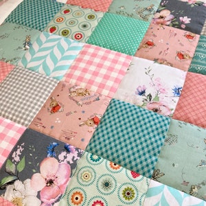 Peut inclure: Une courtepointe en patchwork avec une variété de motifs floraux et géométriques dans des tons de rose, vert et gris. La courtepointe est composée de carrés de tissus différents, chacun avec un design unique. La courtepointe est parfaite pour la chambre d'un bébé ou d'un enfant.