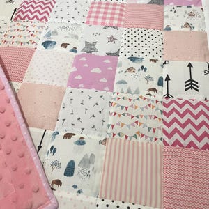 May include: A pink and white patchwork quilt with various patterns, including polka dots, stripes, and geometric designs. The quilt is made of soft, comfortable fabric and is perfect for a baby's nursery.
