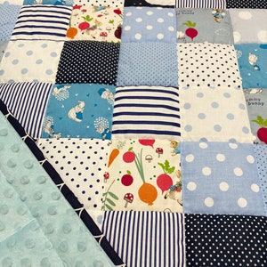 May include: A blue and white patchwork baby quilt with a variety of patterns, including polka dots, stripes, and animal prints. The quilt is made of soft, comfortable fabric and is perfect for cuddling.