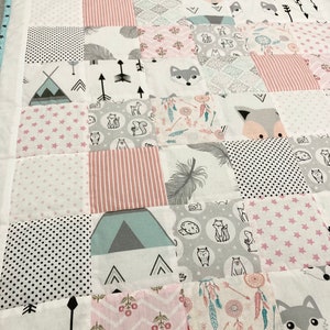 May include: A patchwork quilt with a variety of patterns, including pink and gray stars, arrows, and animal prints. The quilt is made up of squares and rectangles, and the fabric is soft and cuddly.