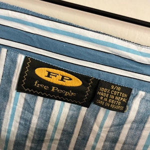 May include: A blue and white striped shirt with a black label that says "free people" and "9/10 100% cotton made in Nepal R.N. 66170 care on reverse".