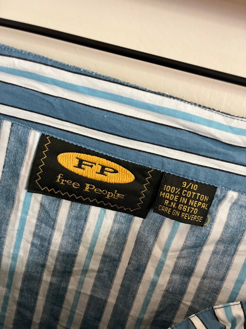 May include: A blue and white striped shirt with a black label that says "free people" and "9/10 100% cotton made in Nepal R.N. 66170 care on reverse".