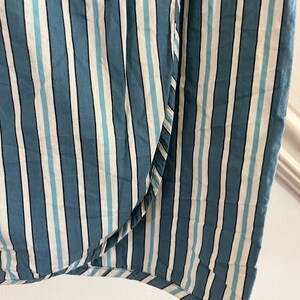 May include: Close-up of a blue and white striped fabric with a subtle sheen. The fabric has a woven texture and a slightly uneven surface.