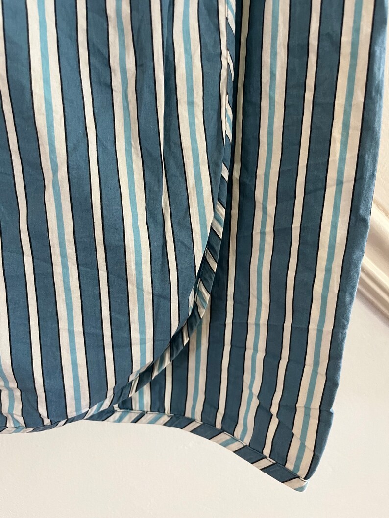 May include: Close-up of a blue and white striped fabric with a subtle sheen. The fabric has a woven texture and a slightly uneven surface.