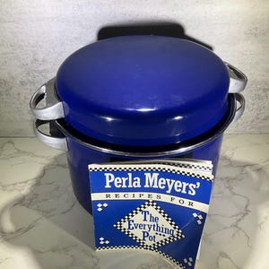 May include: A blue enamel pot with a matching lid and silver handles. A recipe booklet titled "Perla Meyers' Recipes For The Everything Pot" is in front of the pot. The pot is on a white and gray surface.