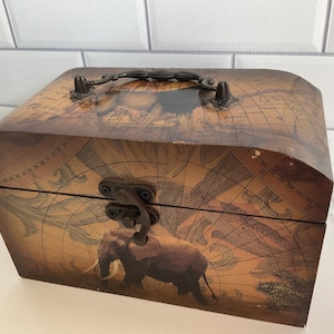 May include: A wooden treasure chest with a map design and an elephant illustration. The chest has a metal handle and clasp. The color scheme is brown and tan.