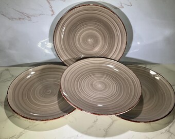 May include: Four ceramic plates with a spiral design in shades of gray and brown. The plates have a rustic, textured appearance with a reddish-brown rim. The plates are arranged on a white surface.