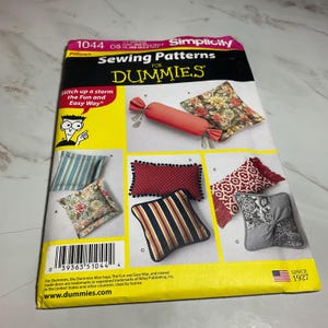 May include: Simplicity Sewing Patterns for Dummies, pattern number 1044, for pillows. The cover features a yellow background with the title and a photo of different pillow designs. The text "Stitch up a storm the Fun and Easy Way" is also included.
