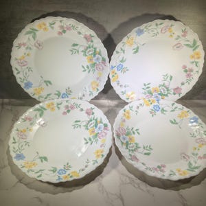 May include: Set of four white dinner plates with a floral pattern in shades of pink, yellow, and blue. The plates have a scalloped edge.