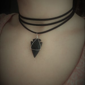 Peut inclure: Un collier ras de cou noir avec un pendentif en argent en forme de pointe de flèche.