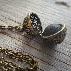 以下が含まれることがあります： フィリグリーペンダントが付いたゴールドトーンのネックレス。ペンダントを開けると、黒い溶岩ビーズが現れます。チェーンは、連結された金属リングで作られています。