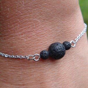 Puede incluir: Un brazalete de cadena plateada con tres cuentas de roca de lava negra.