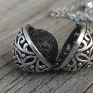 May include: Open silver locket pendant with a black lava rock inside. The locket has a floral design.