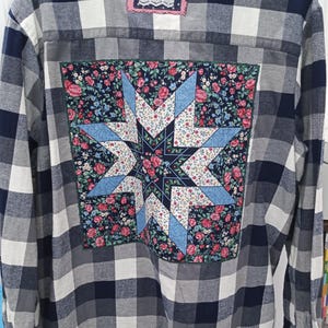 May include: A blue and white plaid flannel shirt with a floral patchwork design on the back. The patchwork design features a star shape in the center.