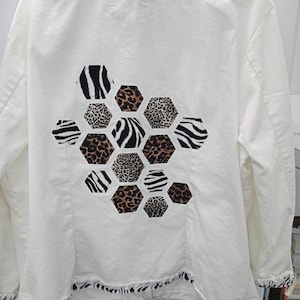 May include: White denim jacket with a black and white zebra print and leopard print design on the back. The design is in the shape of a honeycomb.