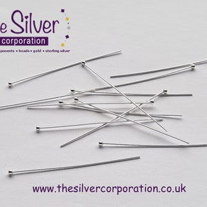May include: A close-up of a pile of silver head pins. The pins are approximately 2.5 cm long and have a small ball at the end. The pins are scattered on a white surface. The text "the Silver corporation" is visible in the top left corner of the image.