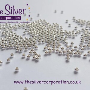 May include: A close-up of a large quantity of small, silver-coloured beads scattered on a white surface. The beads are round and have a smooth, shiny finish. The text "the Silver corporation" is visible in the top left corner of the image.