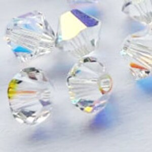 May include: A group of clear glass beads with a faceted, starburst design. The beads have a rainbow iridescent finish.