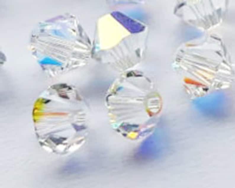 May include: A group of clear glass beads with a faceted, starburst design. The beads have a rainbow iridescent finish.