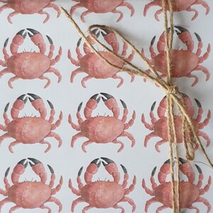 May include: White wrapping paper with a repeating pattern of pink crabs. The paper is tied with twine.