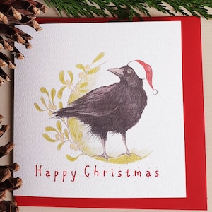Carte de Noël Crow. Drôle de carte de Noël. Corbeau dans un chapeau de père Noël. Carte de Noël avec un chapeau de père Noël. corbeau au gui. carte de Noël oiseau