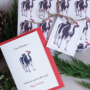 Op de afbeelding: Een rood-witte kerstkaart met een zwart-witte koe die een kerstmanmuts draagt. De kaart staat: "Ik hou van Kerstmis... bijna net zo veel als van de koeien! Fijne Kerst".