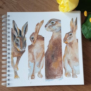 May include: A watercolor painting of four brown hares, each with a different pose. The hares are painted in a realistic style with detailed fur and whiskers.