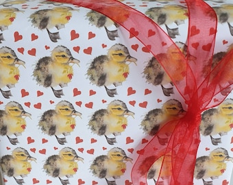 May include: White wrapping paper with a repeating pattern of watercolor ducklings holding red hearts. A red sheer ribbon is tied in a bow on top of the paper.