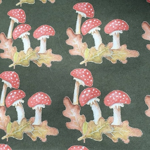 May include: A repeating pattern of red and white mushrooms with white stems on a dark green background. The mushrooms are clustered in groups of three and are surrounded by brown and green leaves.