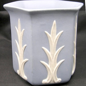 Peut inclure: Un vase en céramique bleu clair de forme hexagonale avec un bord évasé. Le vase présente un motif floral blanc répété sur chaque face. Le vase mesure environ 13 cm de haut.